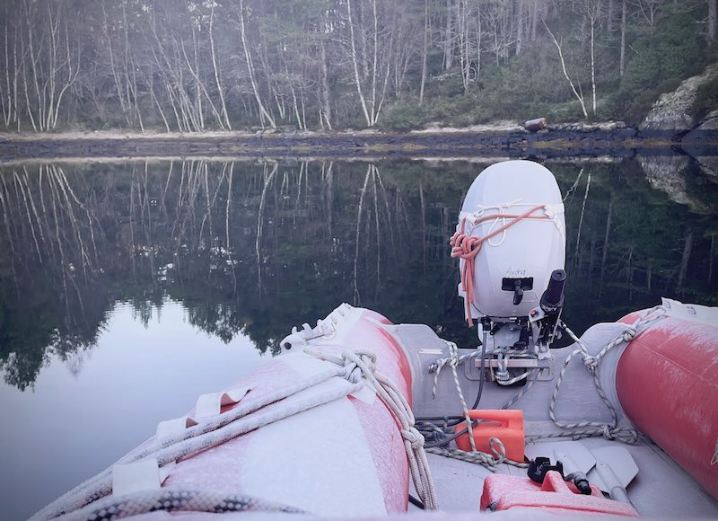 Das vereiste Beiboot vor dem spiegelglatten Meer, ein waldiges Ufer