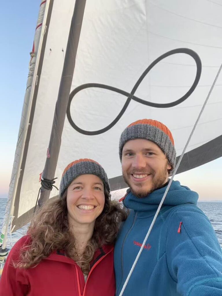 David und StefanieJulia nebeneinander vor dem Segel mit der Lemniskate.