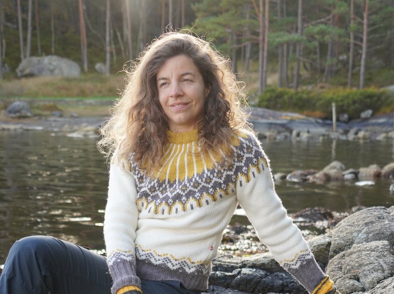 Julia an einer Uferlandschaft mit Wald, sitzend auf einem Stein