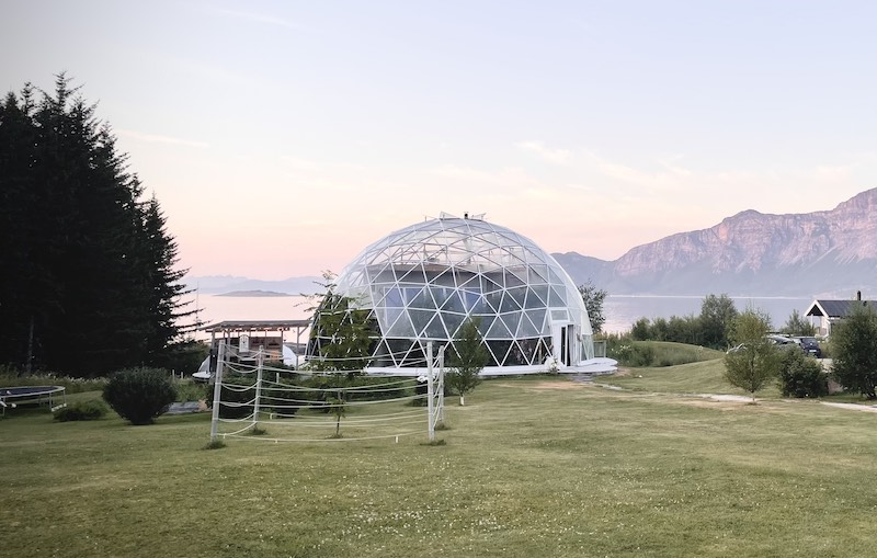 eine geodätische Glaskuppel ist in einer Abendstimmung am Ufer des Meeres zu sehen.