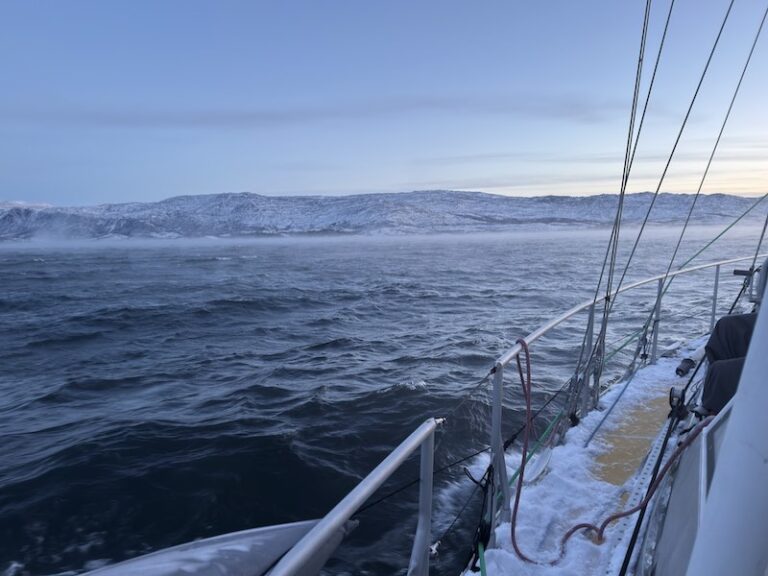 Segelyacht mit gelbem Deck segelt am Polartag, das Meer ist vom Wind und der eisigen Kälte am dampfen.